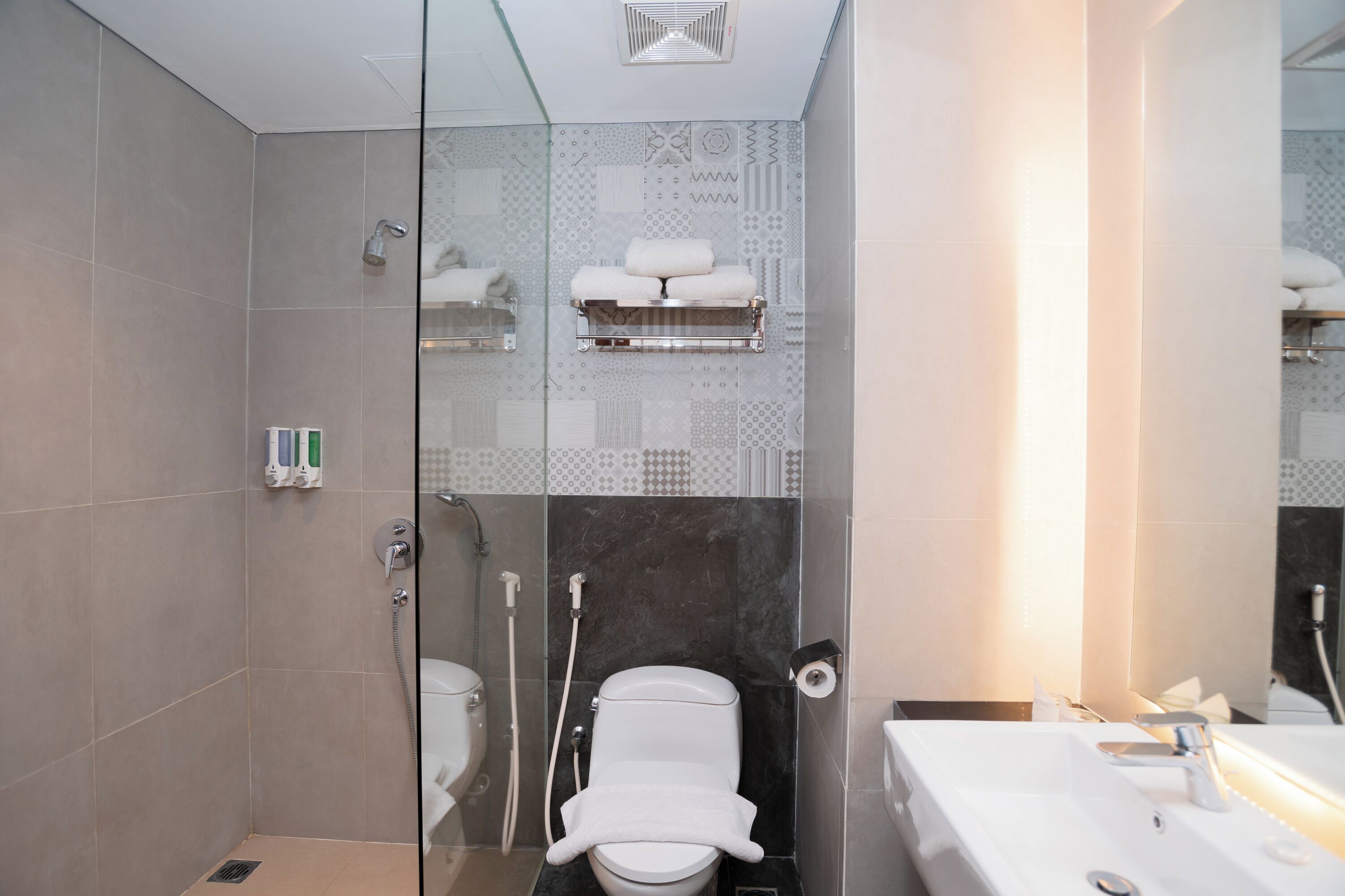 Un baño moderno con cabina de ducha de vidrio, inodoro con barra para toallas y lavabo con espejo.