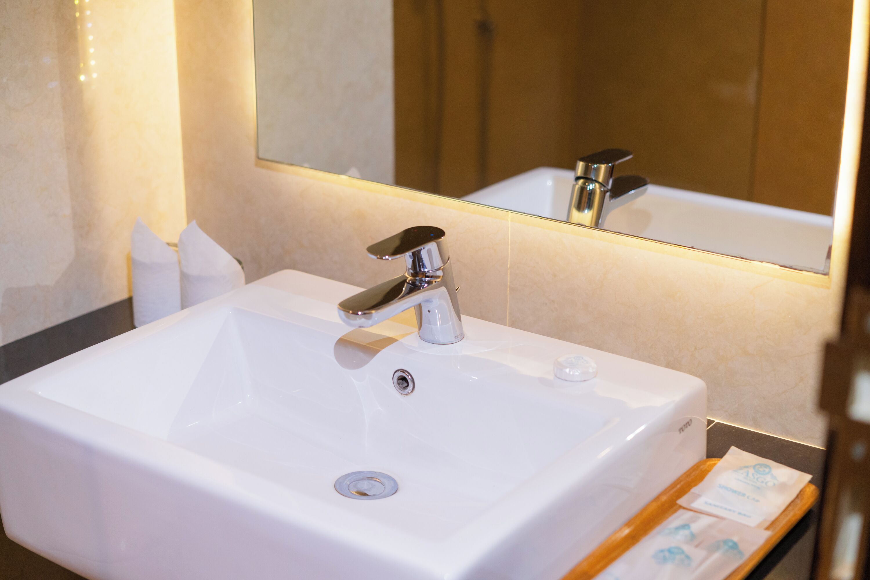 Un baño de hotel con un lavamanos blanco, un espejo y un dispensador de toallas.