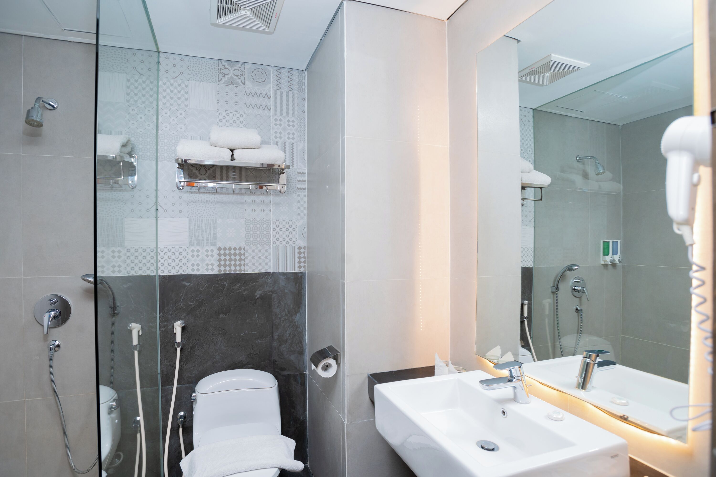 Ein modernes Badezimmer mit einer gläsernen Dusche, einer weißen Toilette, einem Waschbecken mit Spiegel und einem Handtuchhalter mit Handtüchern.