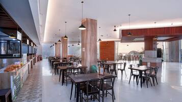 En rummelig restaurant med højt til loftet, synlige træbjælker og moderne hængende lamper. Bordene og stolene er anrettet til spisning.