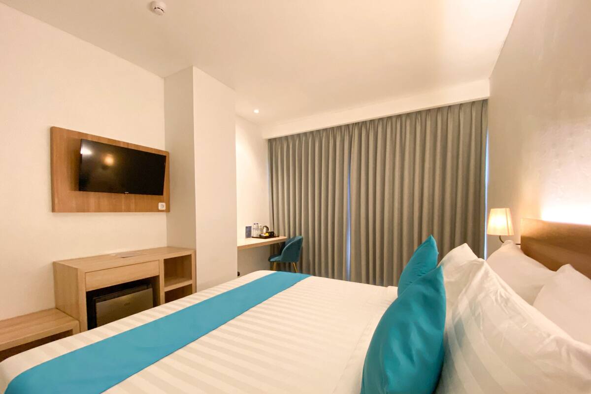A hotel room with a large bed, a desk, a chair, a television, and a window with curtains.