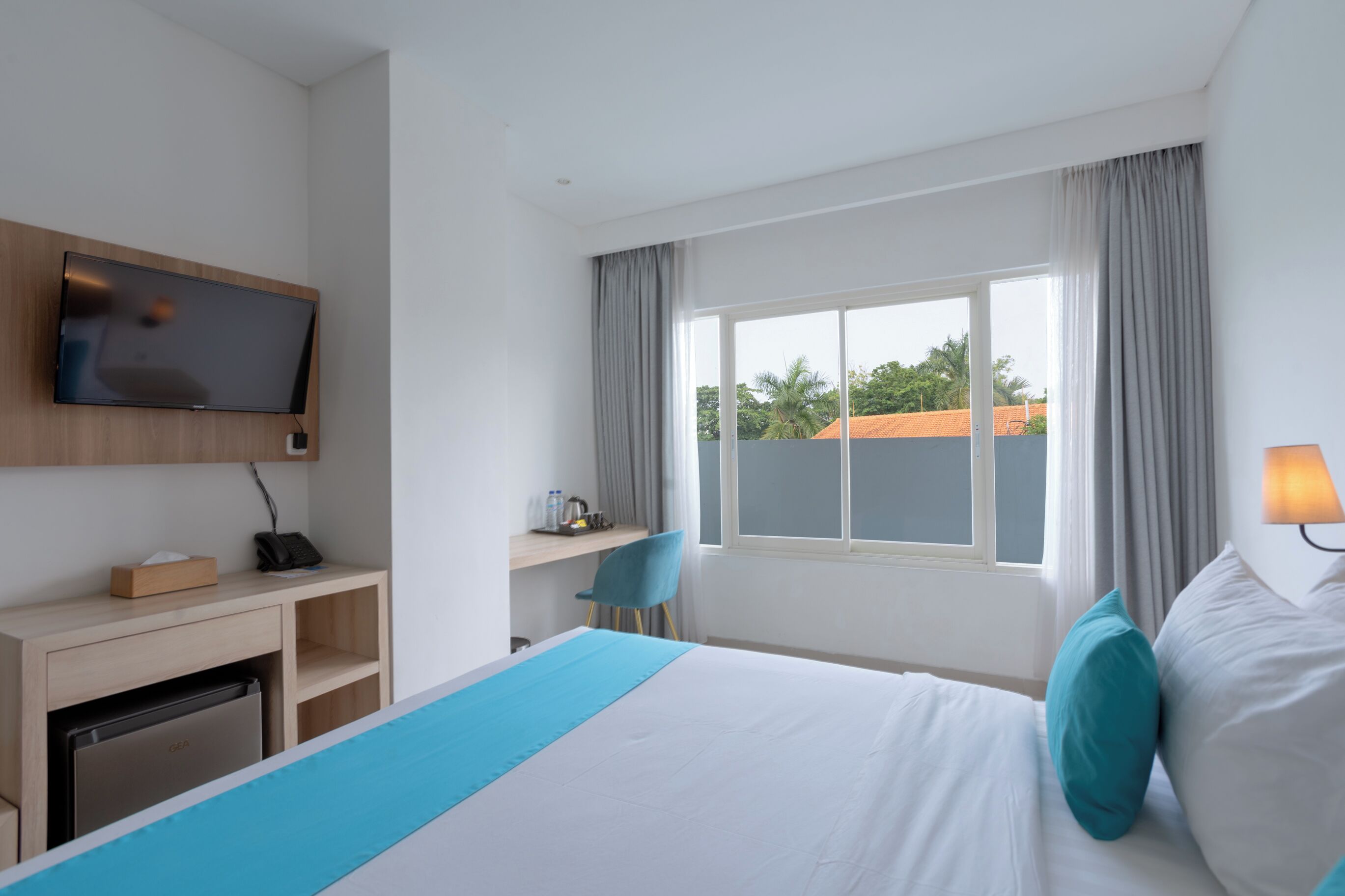 Une chambre d’hôtel avec un lit, un bureau équipé d’un ordinateur, un téléviseur fixé au mur et une fenêtre avec des rideaux.