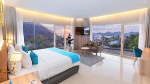 A modern hotel room with a large bed, a TV, a sofa, and a view of the city. - ZASGO HOTEL (Labuan Bajo)