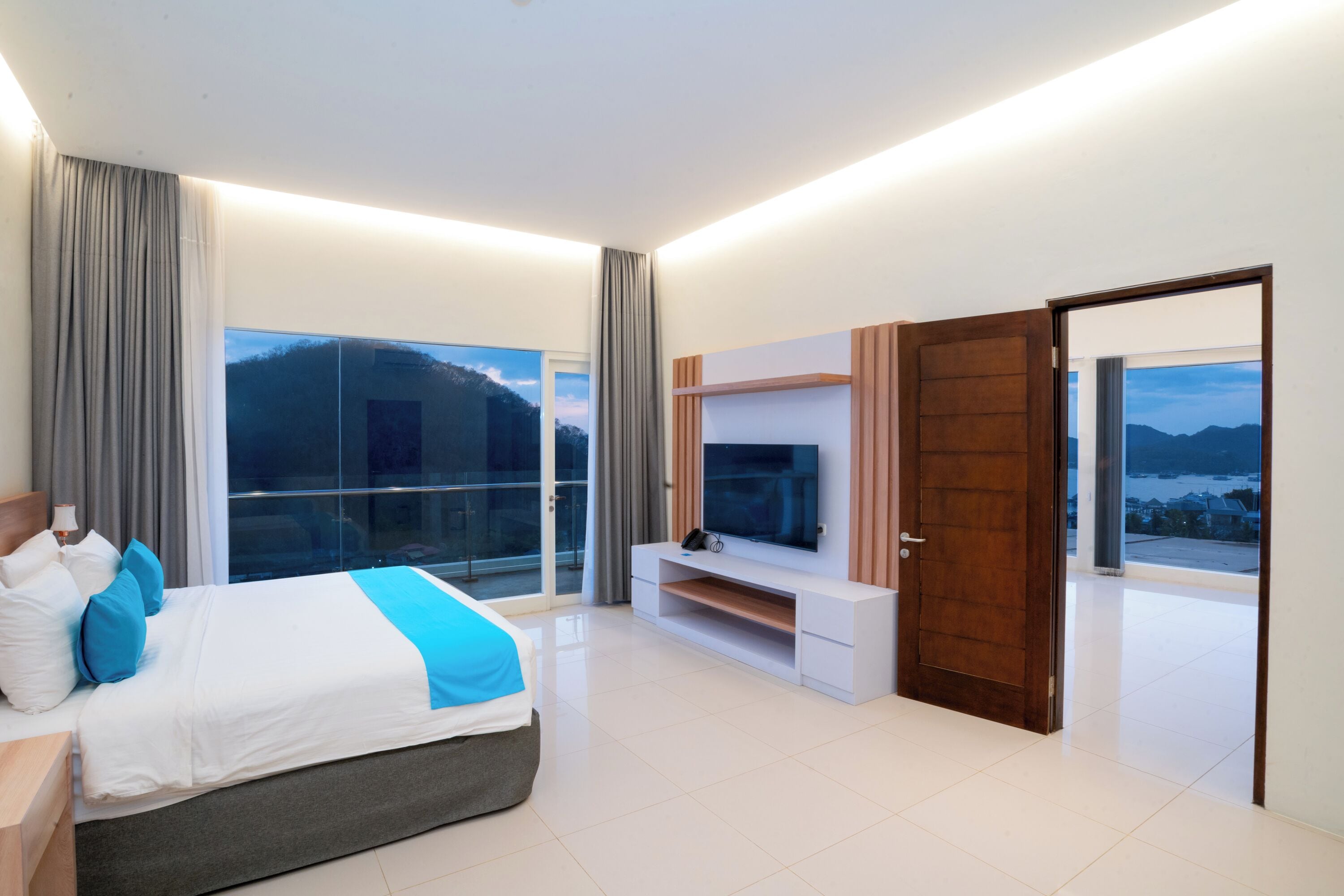 Une chambre d’hôtel moderne dotée d’un grand lit, d’une télévision et d’un balcon offrant une vue sur la montagne.