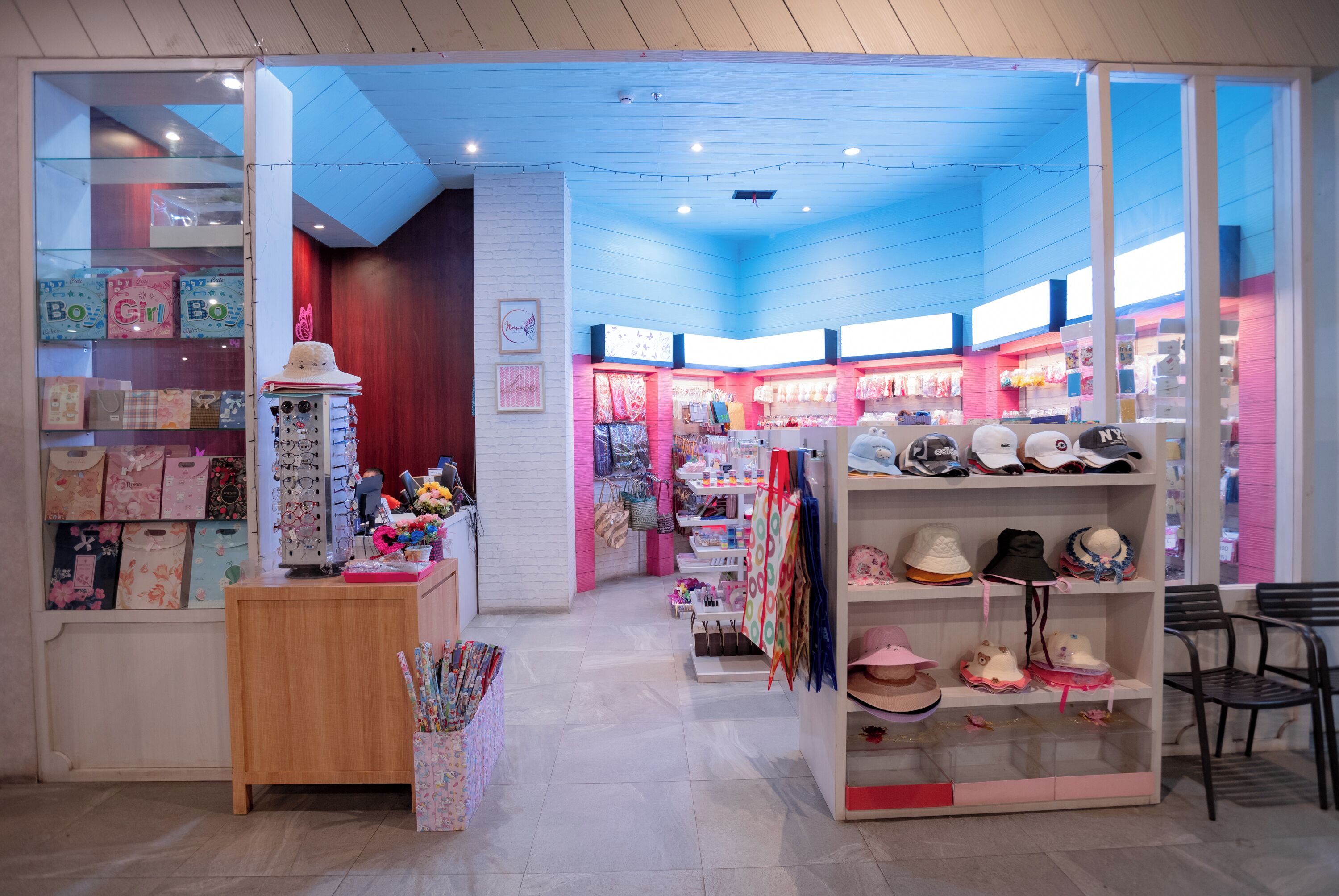 Un magasin bien éclairé, avec des étagères remplies de chapeaux et de sacs, un comptoir en bois et un présentoir de papeterie aux couleurs vives.