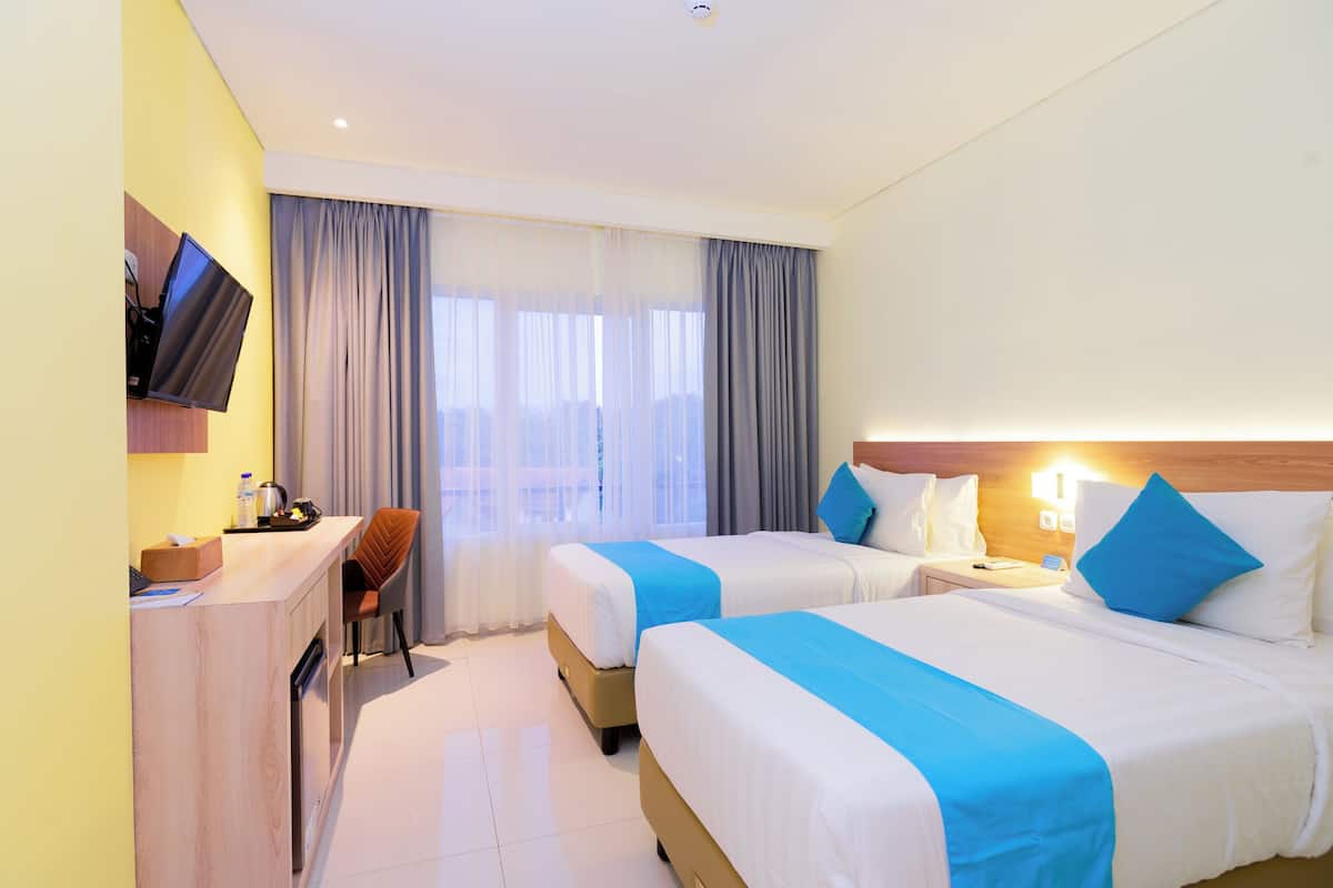 A hotel room with two beds, a desk, a chair, a TV, and a window with curtains.