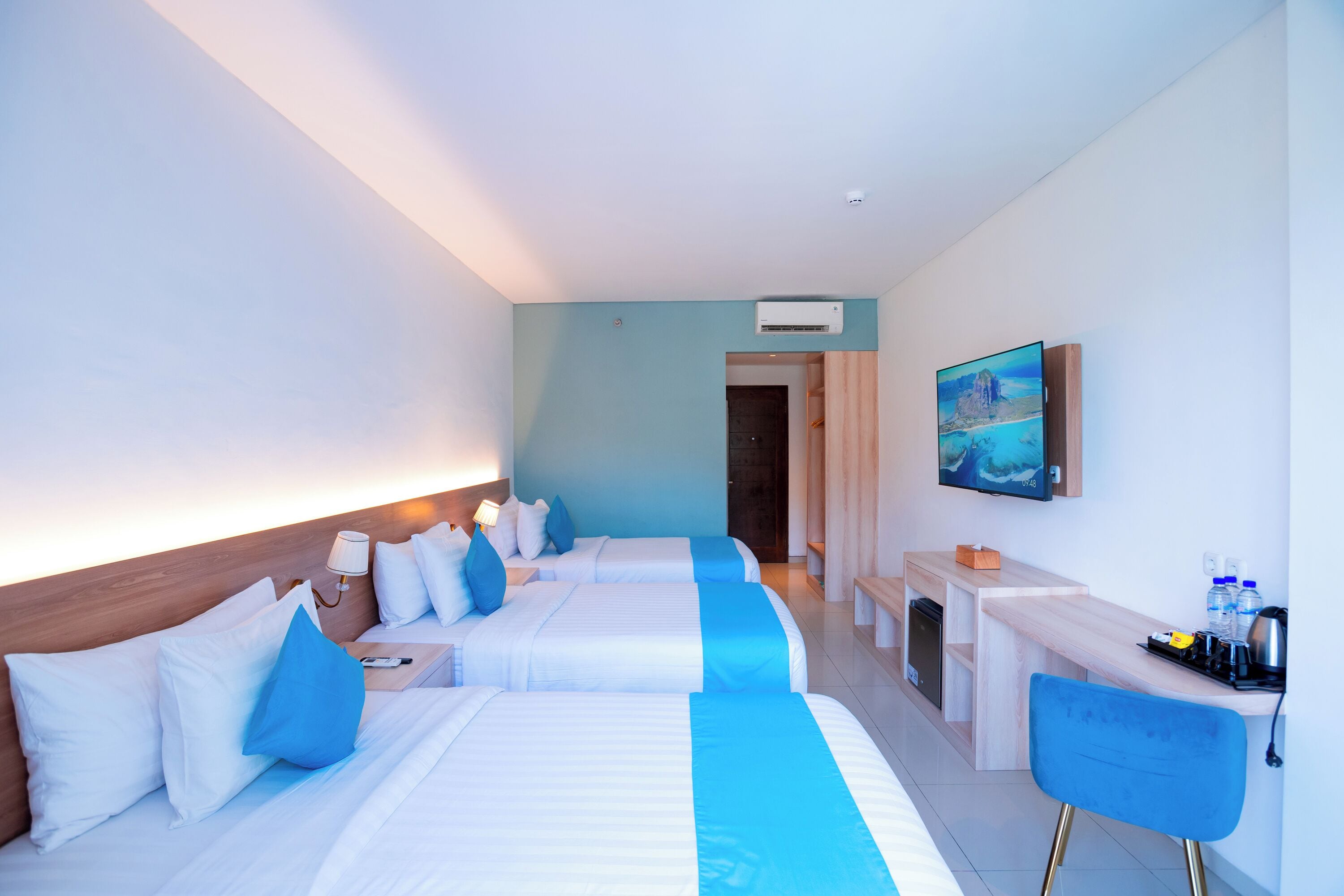A hotel room with two beds, a desk, a chair, a TV, and a bathroom.