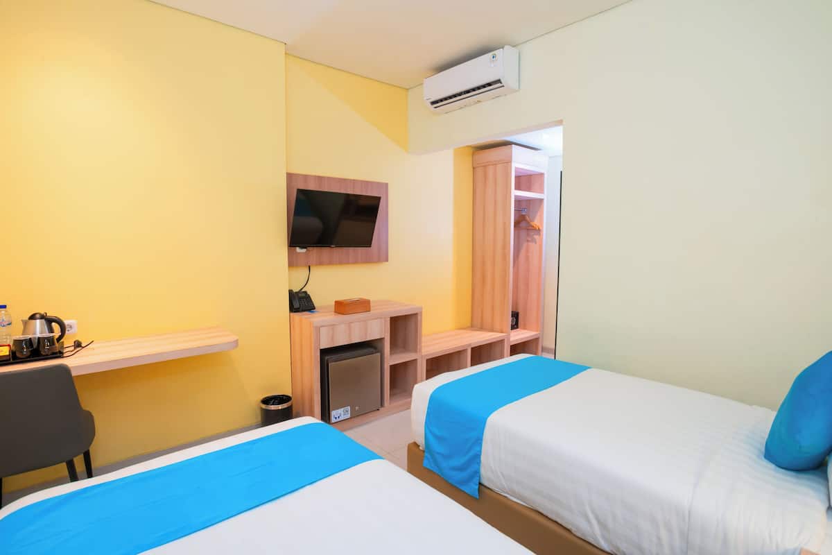 A hotel room with two beds, a desk, a TV, a mini-fridge, and a wardrobe.