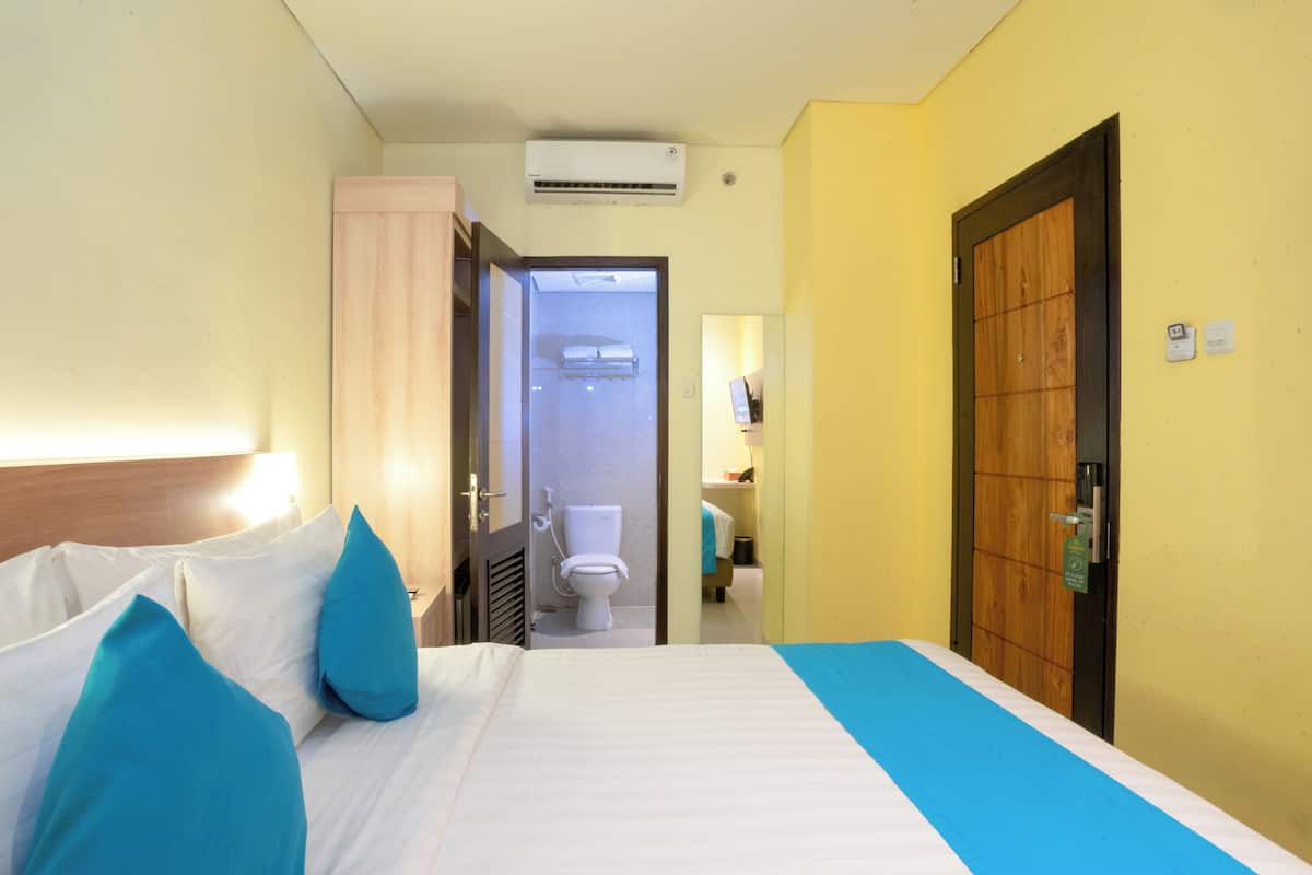 A hotel room with a bed, a wooden door, and a bathroom visible through an open door.