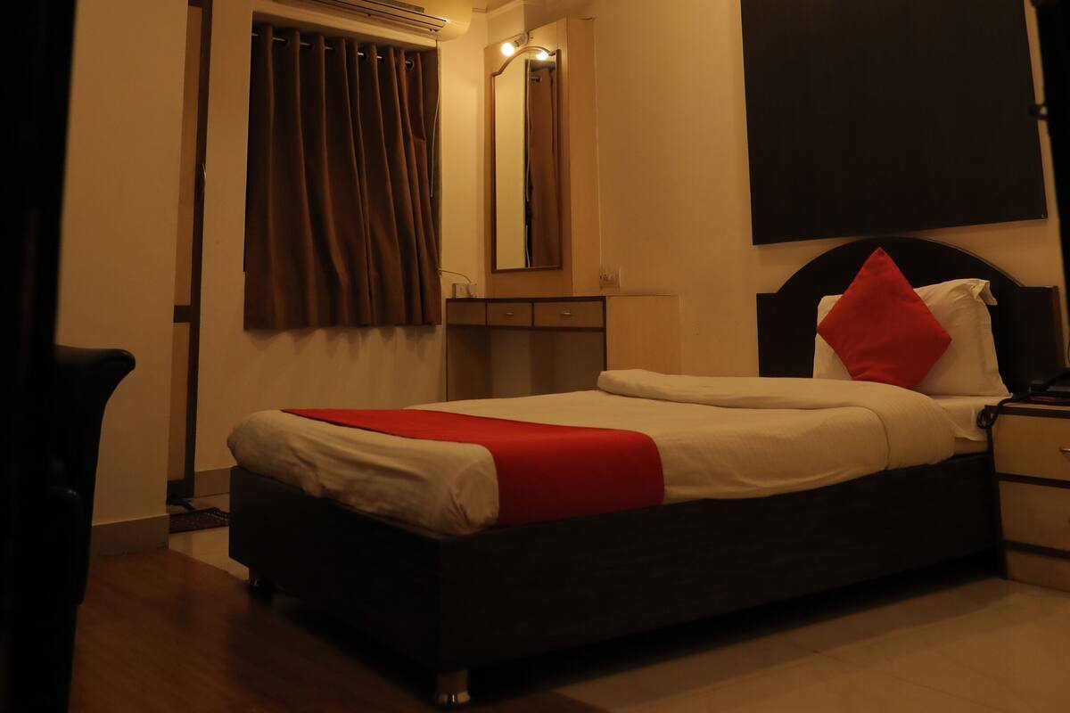 A bedroom with a bed, a ceiling fan, an air conditioning unit, a nightstand, and a mirror.