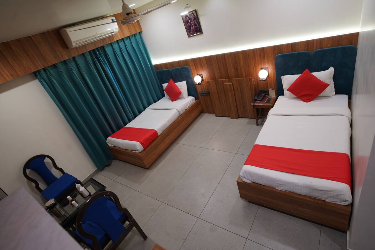 A hotel room with two beds, a desk, chairs, and an air conditioning unit.