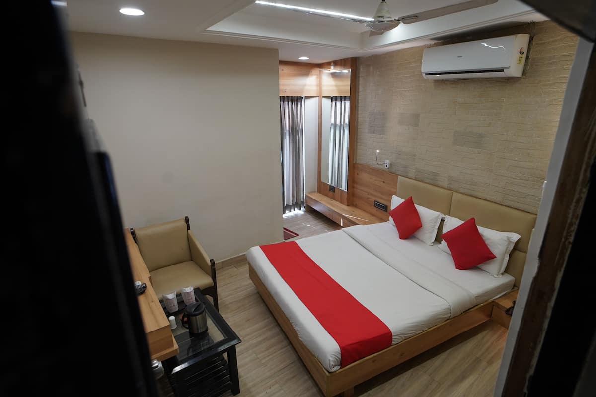 A hotel room with a bed, a desk, a chair, and an air conditioning unit.