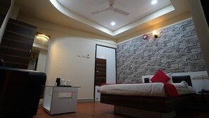 A modern bedroom with a bed, a desk, and a ceiling fan. - Hotel Gokul (Gandhidham)