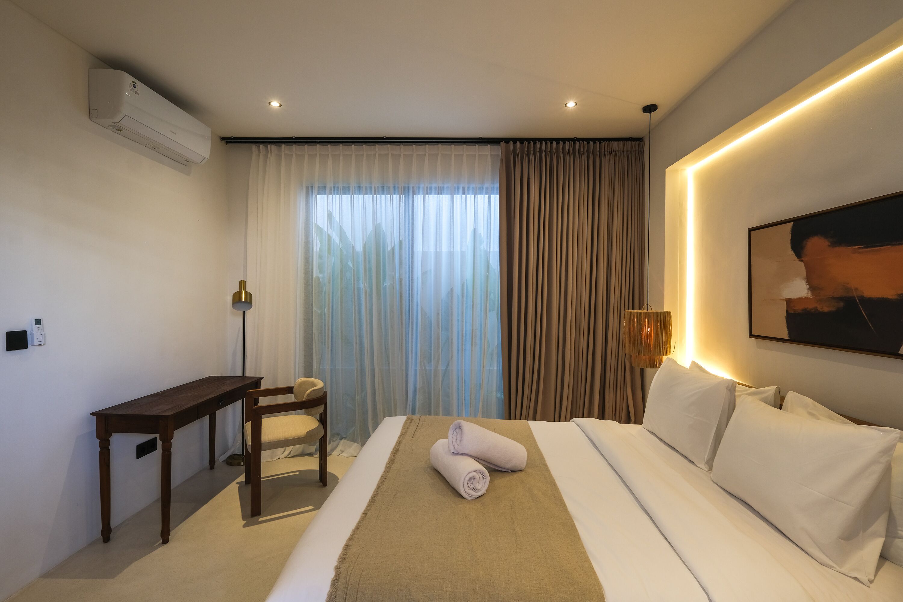 A hotel room with a bed, a desk, a chair, a lamp, and a painting on the wall.