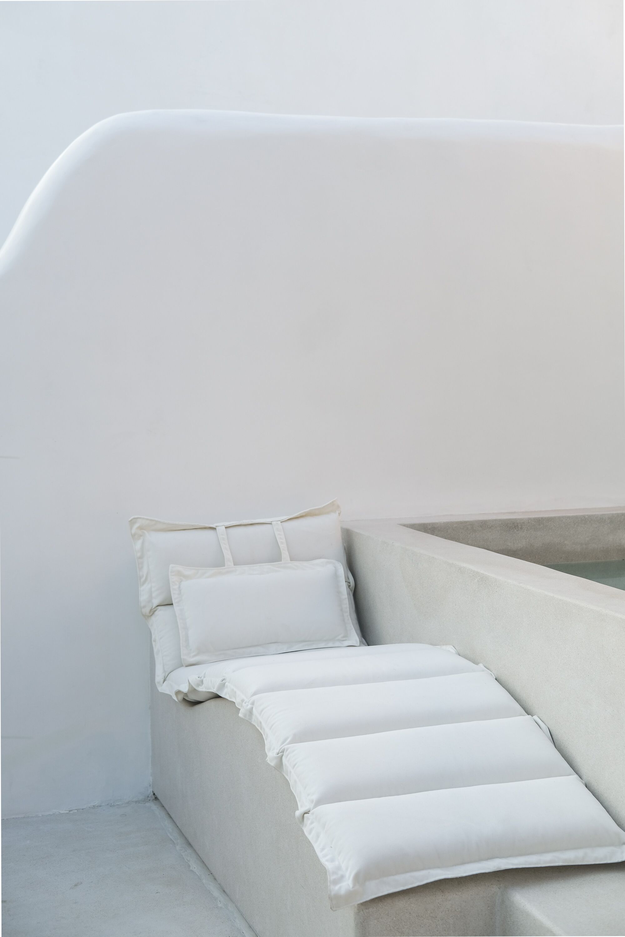 A minimalist room with a bed, pillows, and a concrete wall.
