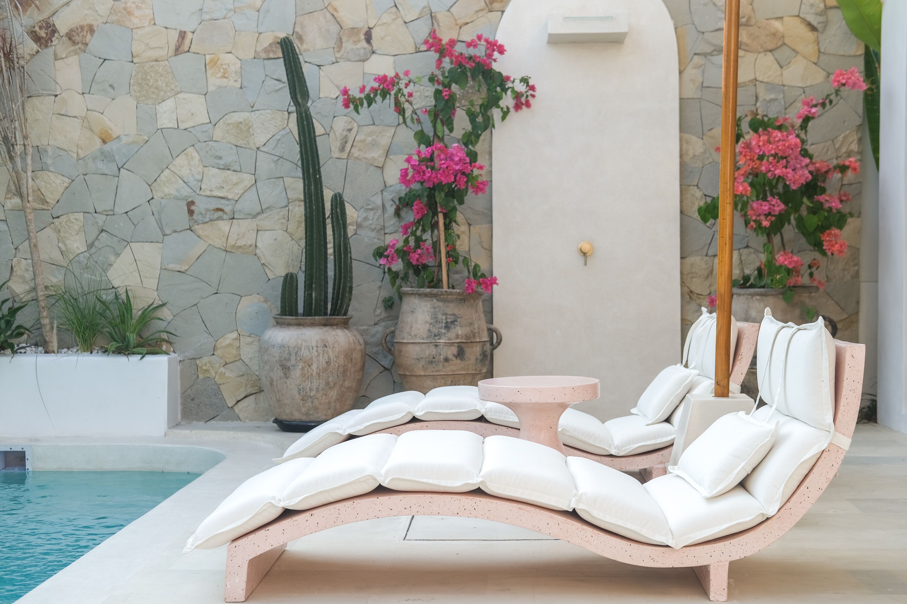 A poolside lounge with a curved white cushioned chair, a small round table, and potted plants.