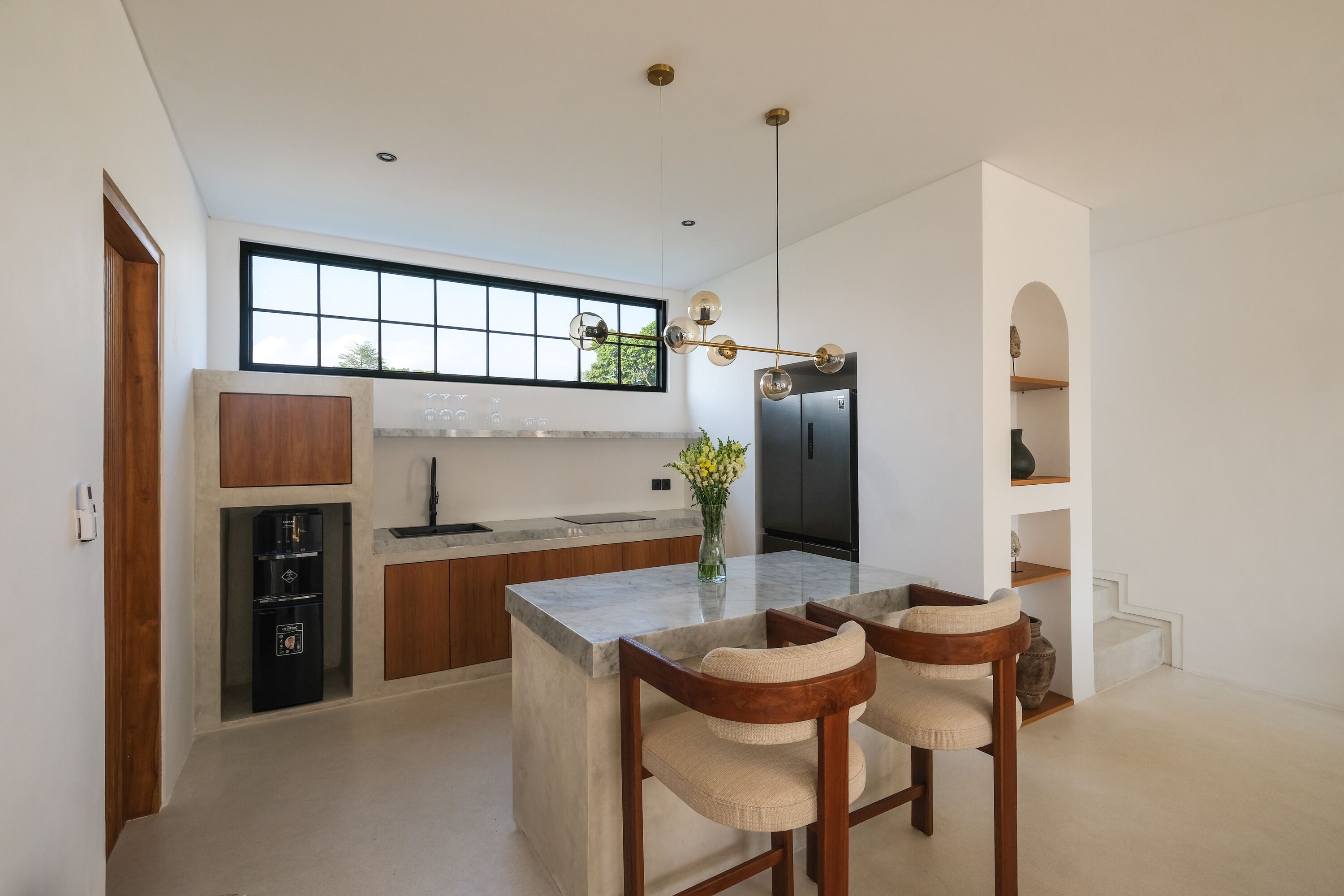 Una cocina moderna con una isla grande, taburetes de bar, una cafetera empotrada y un ventanal amplio.