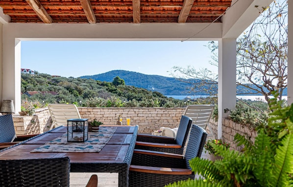 An outdoor patio with a table and chairs, a view of a mountainous landscape, and a body of water in the distance. - Nice home in Vela Luka with WiFi (Vela Luka)