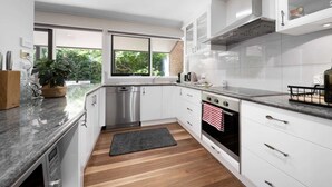 Cocina moderna con armarios blancos, electrodomésticos de acero inoxidable y un amplio ventanal con vistas a zonas verdes.