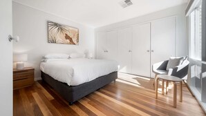 Un dormitorio con cama, mesita de noche, silla, armario y ventana.