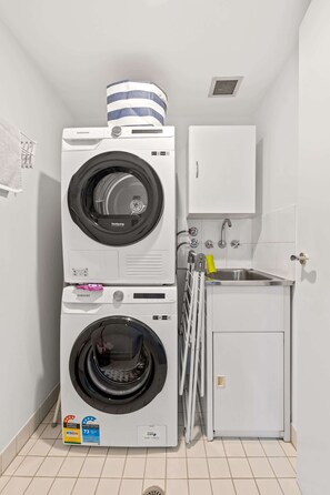 A compact laundry room with stacked washing machines, a small sink, and a cabinet.