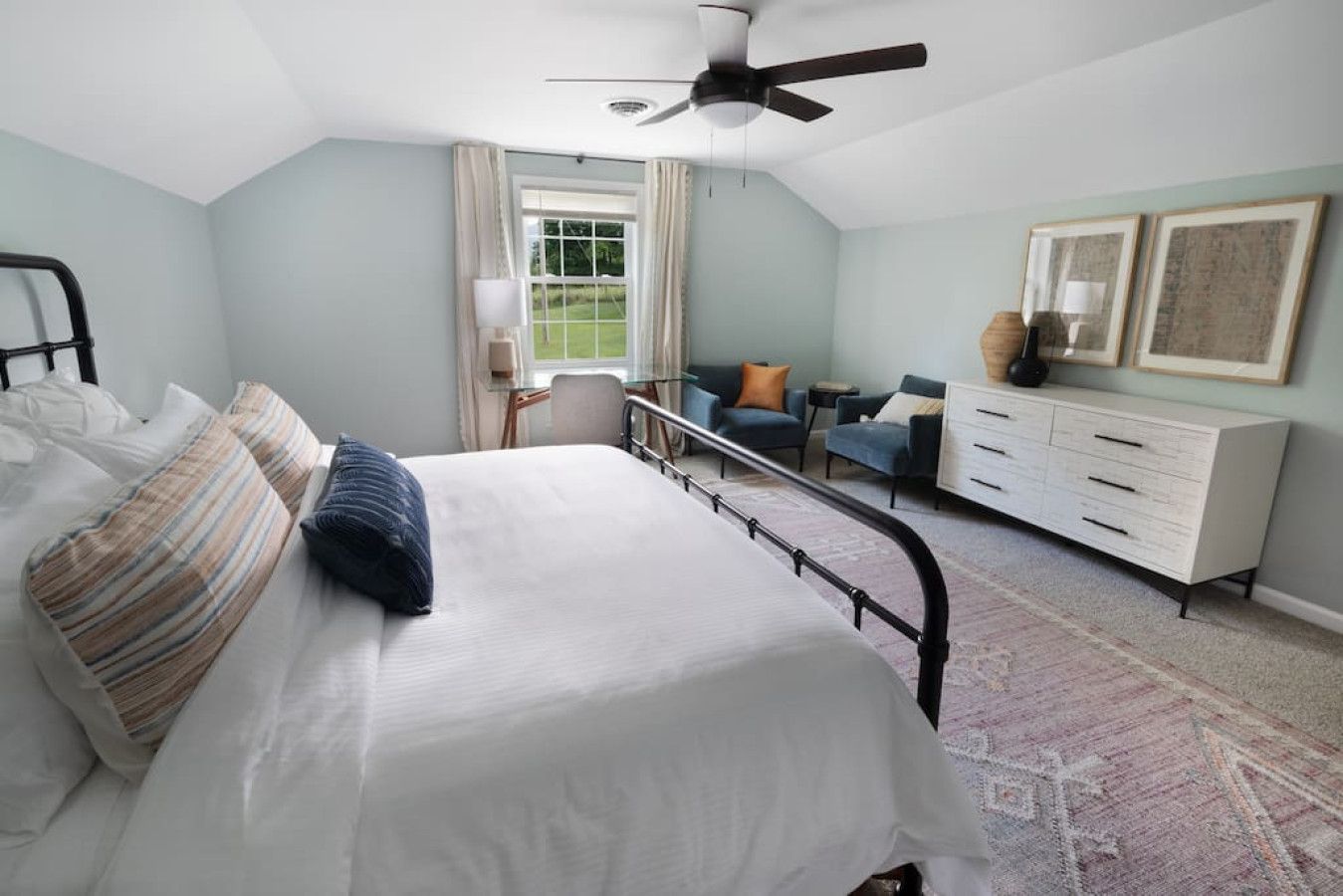 A bedroom with a bed, a desk, a chair, a dresser, and a ceiling fan.