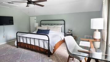 A bedroom with a bed, a desk with a chair, a ceiling fan, and a window with curtains.