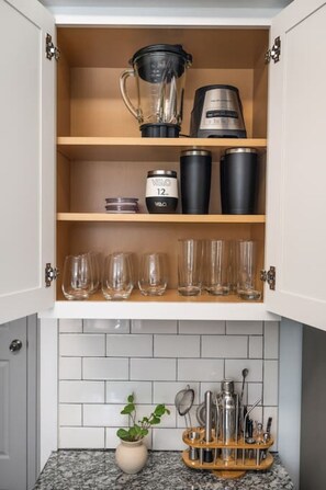 Un armario de cocina con una licuadora, cafetera y cristalería.