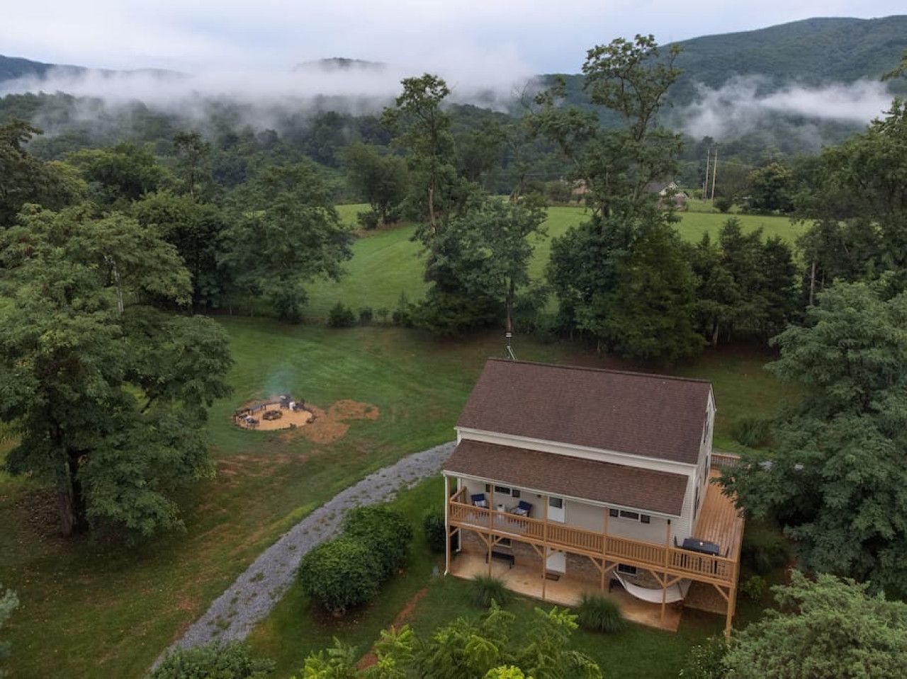 A two-story house with a deck and a covered outdoor area, surrounded by dense forest and hills.