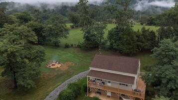 A two-story house with a deck and a covered outdoor area, surrounded by dense forest and hills.