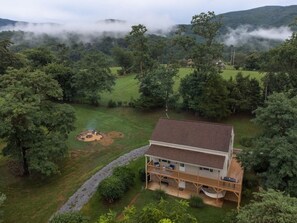 A two-story house with a deck and a covered outdoor area, surrounded by dense forest and hills. - Charming Cottage w/ Incredible Views & Firepit (Stanley)