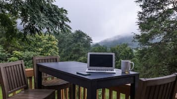 Een houten terras met een tafel, stoelen, een laptop en een mok.
