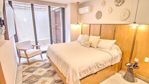 A hotel room with a large bed, a chair, a small table, and decorative wall art. - Arenka: 2BR w Private Pool & Sunset Rooftop (Bucerías)