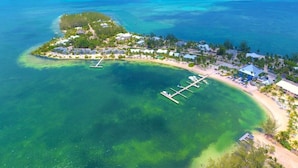 An aerial view of a coastal resort with clear turquoise waters, a marina, and a variety of buildings.
