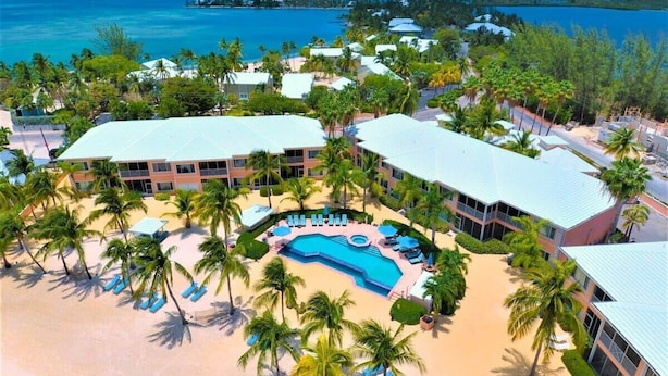 A resort with a central pool, palm trees, and beachfront views.