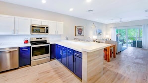 A modern kitchen with white cabinets, a built-in microwave, and an oven. There is a dining area with a wooden table and chairs.