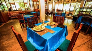 A restaurant with tables covered in blue tablecloths, wooden chairs, and a central pillar. - Surf Sea Breeze (Mirissa)