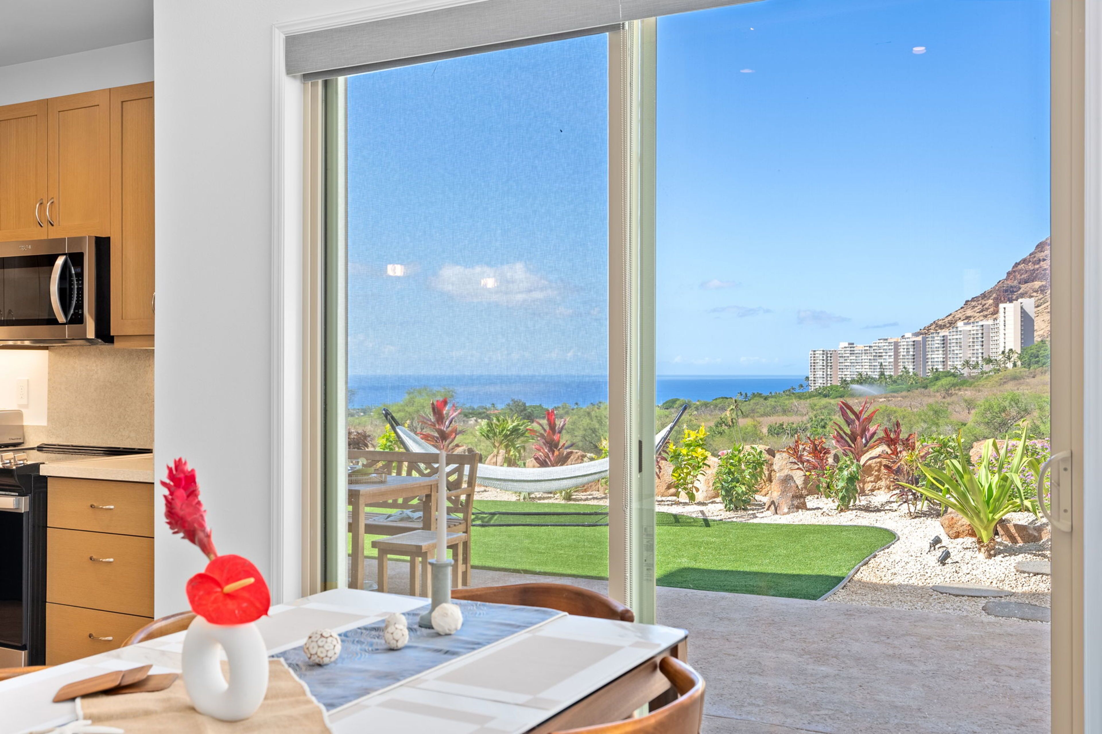 A modern kitchen with a large sliding glass door leading to a patio with a view of the ocean and a garden.