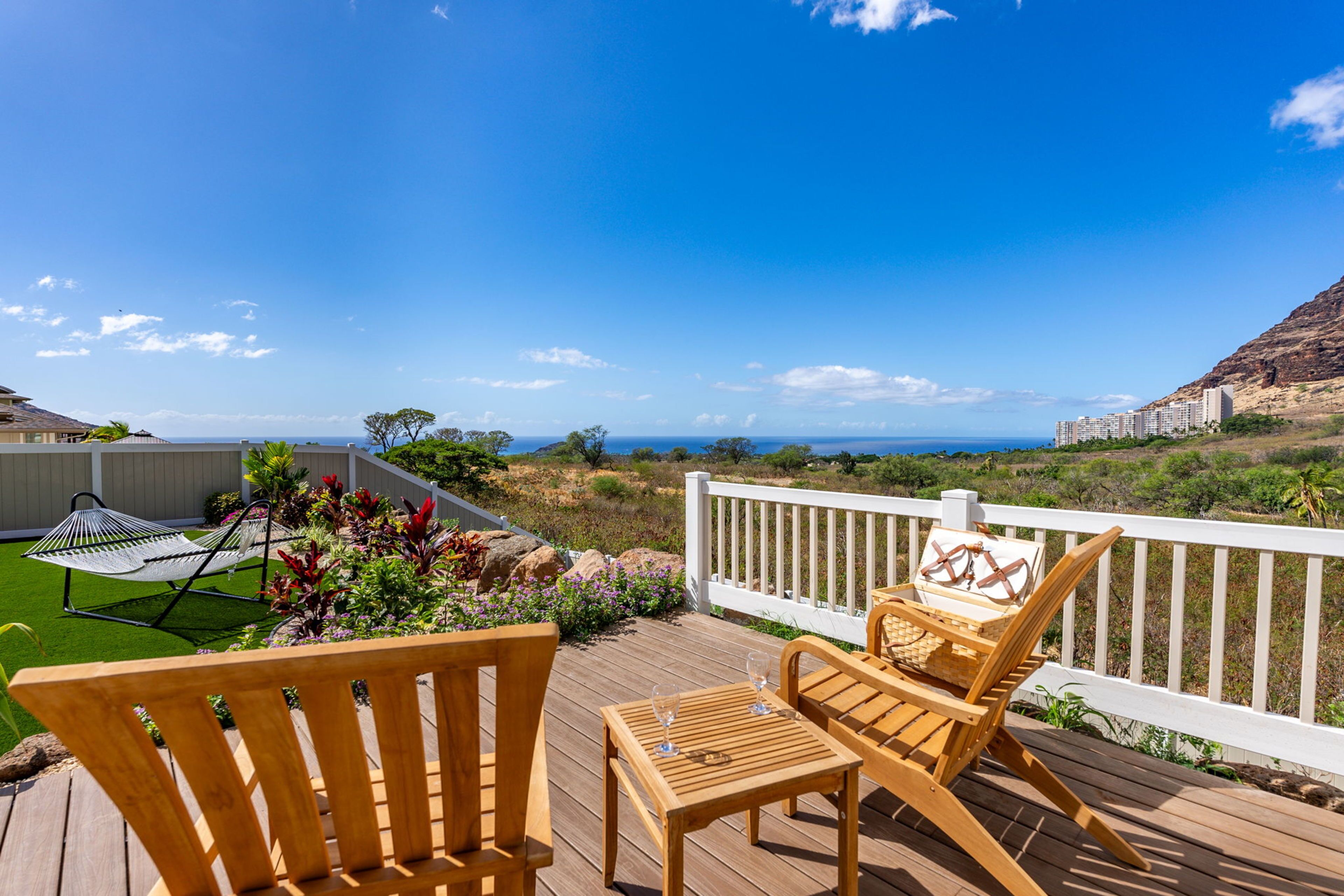 A wooden deck with two chairs and a table, overlooking a coastal landscape with a clear sky.