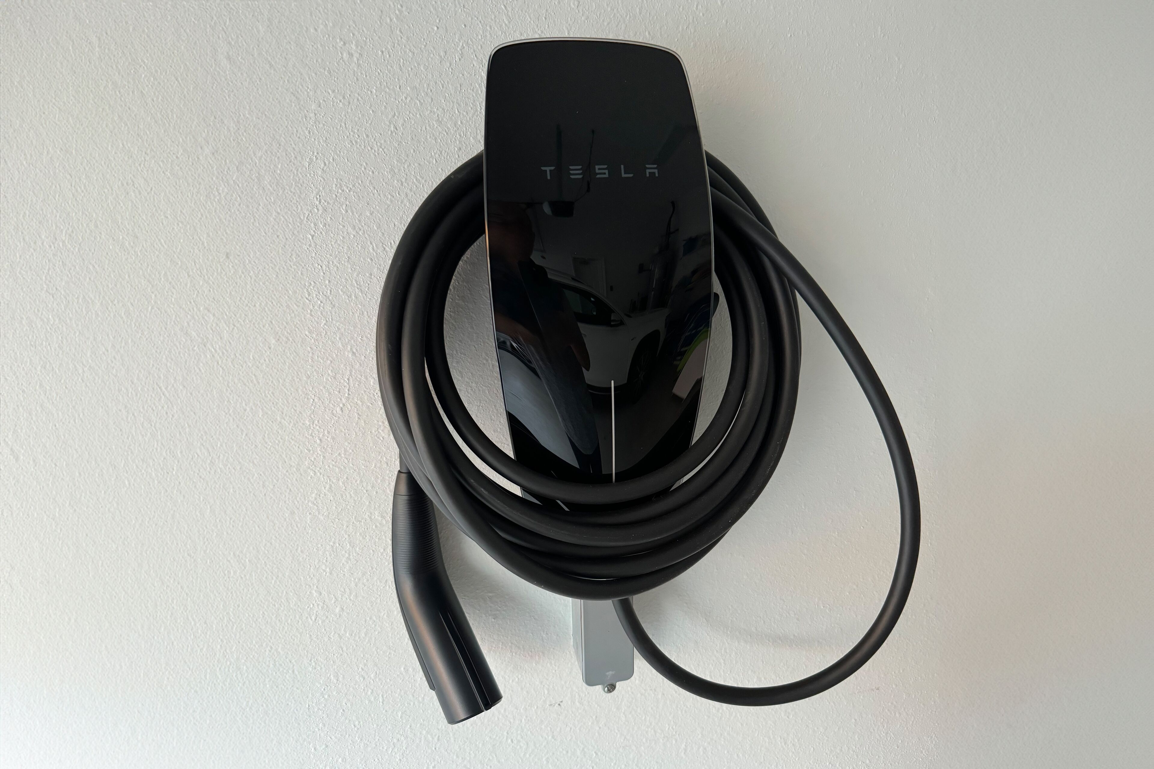 A Tesla charging station with a cable coiled around it.