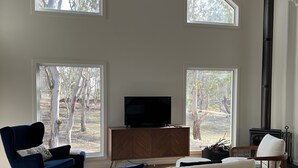 A spacious living room with a high ceiling, large windows, a fireplace, and a television. - Beautiful Country Home.  5 min to Armidale, 10 min to University of New England. (Armidale)