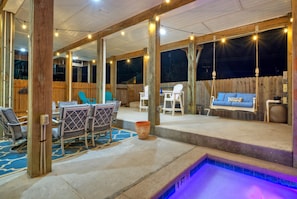 An outdoor patio with a pool, wooden deck, and seating area with chairs and a swing.