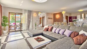 A modern living room with a sectional sofa, a coffee table, and a dining area with a chandelier. - Gorgeous home in Pula (Pula)