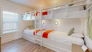 A bunk bed room with white bedding and orange accents, a window with blinds, and a wooden floor. - Golf Cart Included, Pet Friendly, Shared Pool, Parking for 1 Vehicle (Port Aransas)