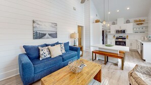 A modern living room with a blue sofa, wooden coffee table, and a ceiling fan. - Golf Cart Included, Pet Friendly, Shared Pool, Parking for 1 Vehicle (Port Aransas)
