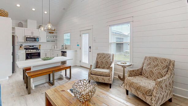 A spacious kitchen with white cabinetry, a wooden bench, and a dining table. There is a patterned armchair and a small round table with a decorative item on it. - Golf Cart Included, Pet Friendly, Shared Pool, Parking for 1 Vehicle (Port Aransas)