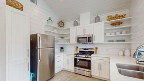 A modern kitchen with white cabinetry, stainless steel appliances, and decorative items. - Golf Cart Included, Pet Friendly, Shared Pool, Parking for 1 Vehicle (Port Aransas)