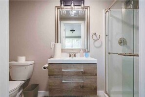 Bathroom features a toilet, vanity with two drawers, and a glass shower enclosure.
