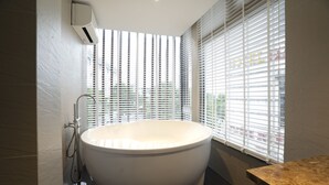 Un baño moderno con una bañera independiente, cabezal de ducha y una ventana con persianas.