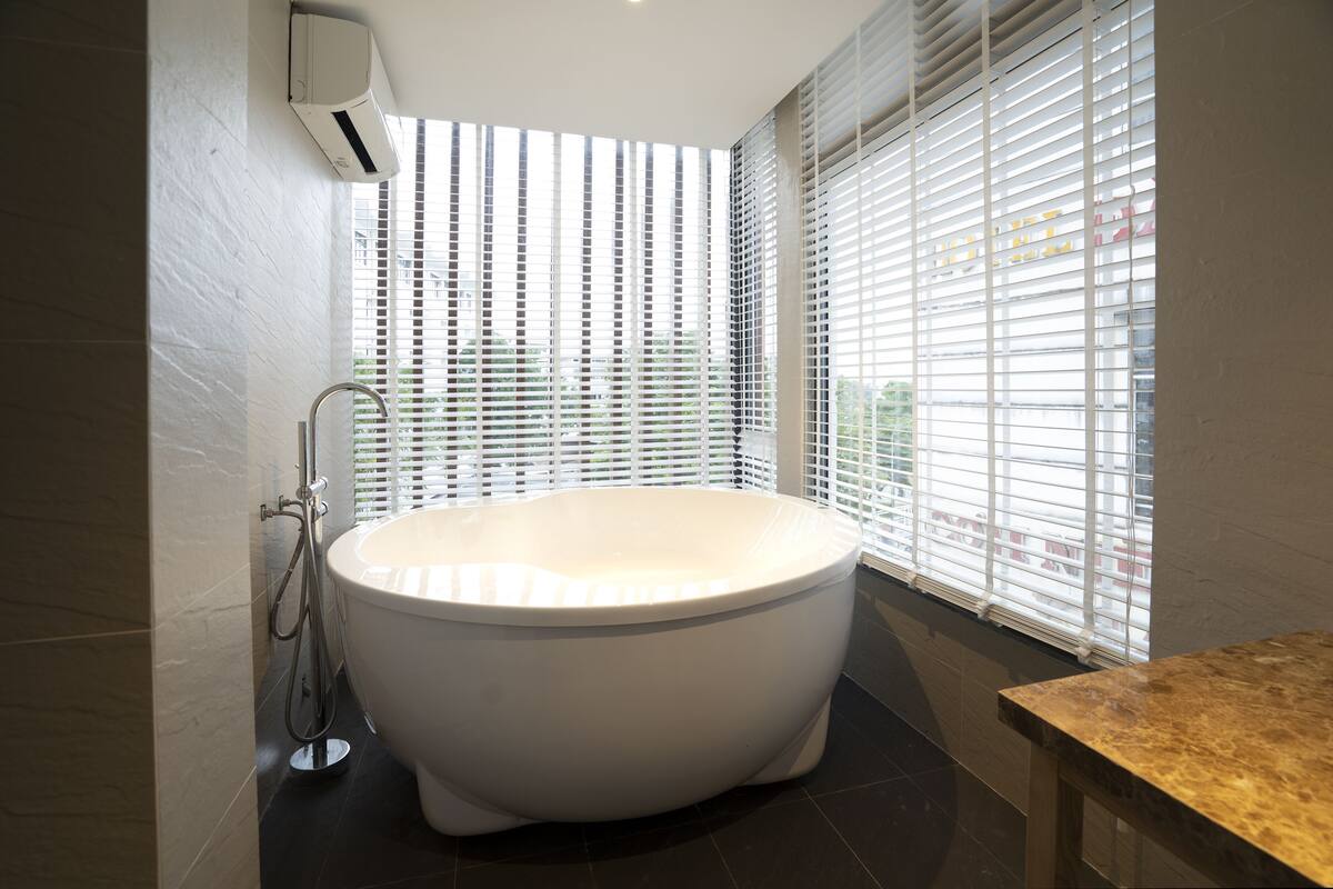 A modern bathroom with a freestanding bathtub, a showerhead, and a window with blinds.